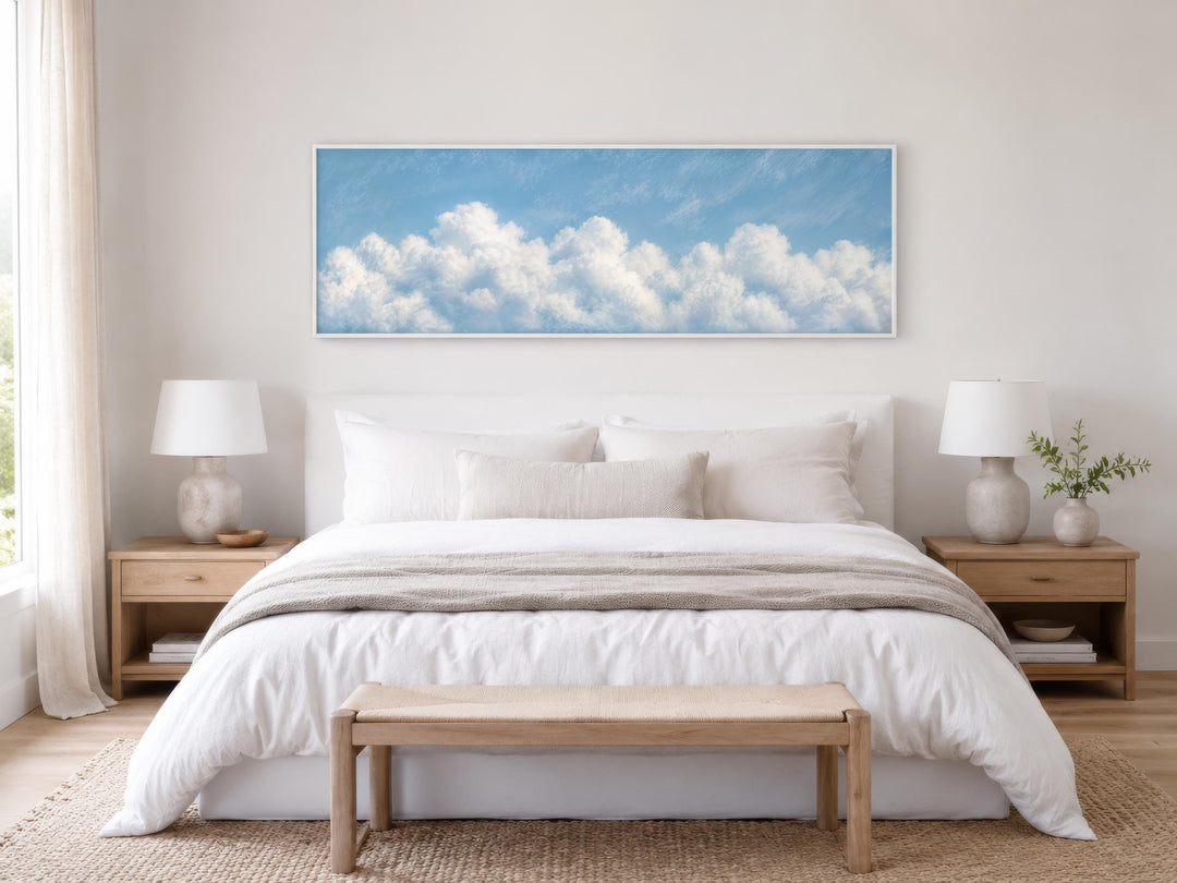 Long horizontal white cloud painting on blue sky canvas above a bed in a coastal bedroom.