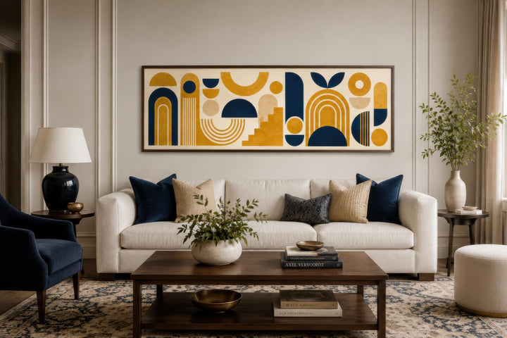 Long narrow canvas wall art with mustard yellow and navy blue Bauhaus geometric shapes over a sofa.