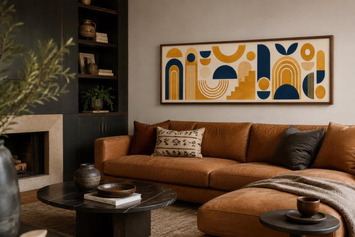 Long narrow Bauhaus canvas wall art with mustard yellow and navy geometric shapes above a tan sofa.
