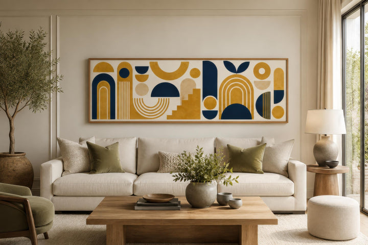 Long narrow Bauhaus canvas wall art with mustard yellow and navy blue geometric shapes above a sofa.