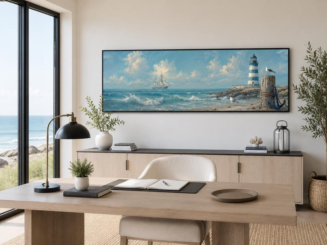 Long nautical canvas print of a sailing ship and lighthouse above a desk in a coastal office.