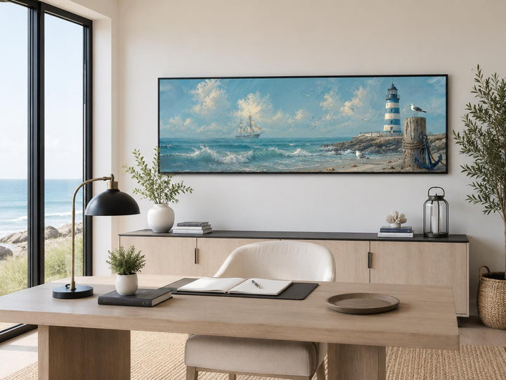 Long nautical canvas print of a sailing ship and lighthouse above a desk in a coastal office.