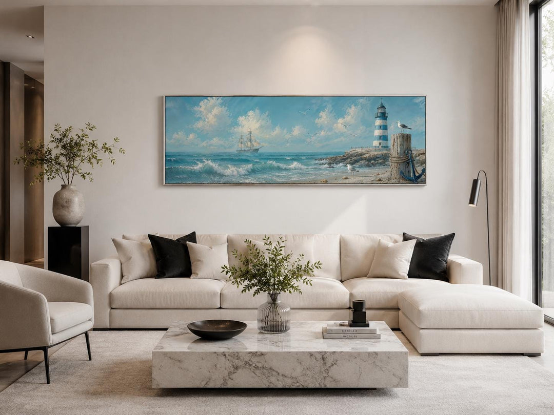 Long horizontal canvas print of a sailing ship and lighthouse above a modern white sectional sofa.