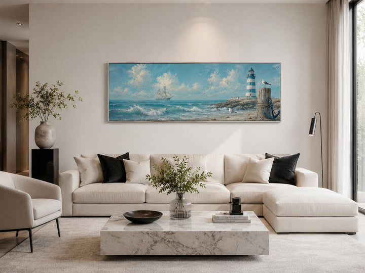 Long horizontal canvas print of a sailing ship and lighthouse above a modern white sectional sofa.