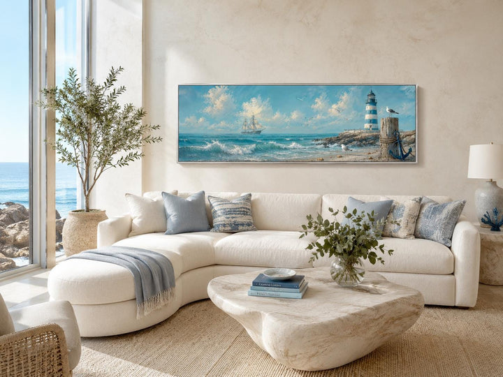 Long sailing ship and lighthouse canvas print above a white sofa in a coastal living room.
