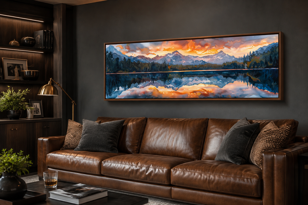 Panoramic framed canvas wall art of a sunset over a mountain lake above a brown leather sofa.