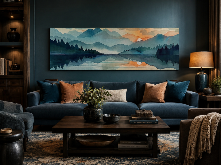 Long horizontal watercolor mountain lake sunset canvas wall art above a blue sofa in a living room.