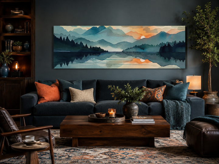 Long horizontal watercolor mountain lake sunset canvas wall art above a dark blue sofa.