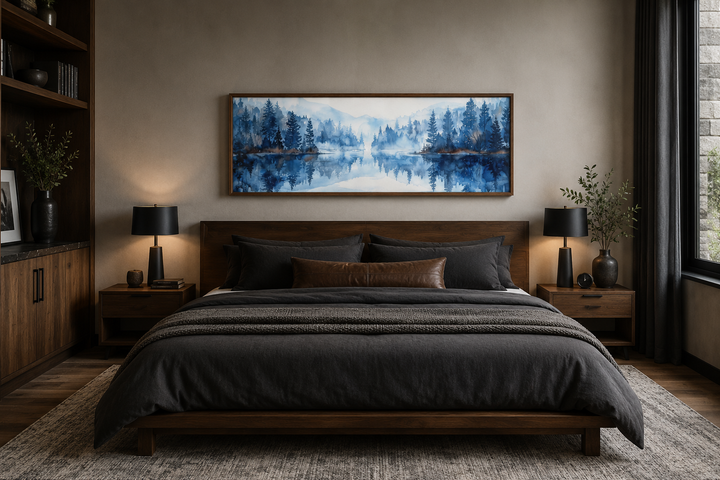 Navy blue lake watercolor landscape painting in a wood frame above a dark wood bed.