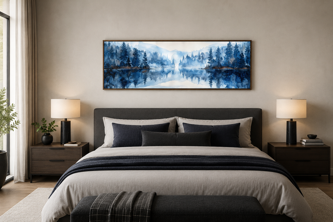 Navy blue lake watercolor landscape painting in a long narrow frame above a bed.