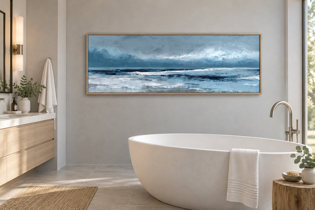 Long horizontal abstract blue ocean canvas wall art in a light wood frame above a bathtub.