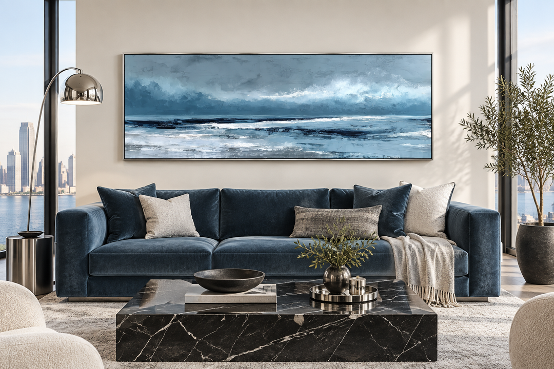 Long horizontal light blue abstract ocean canvas wall art hanging above a navy blue velvet sofa.