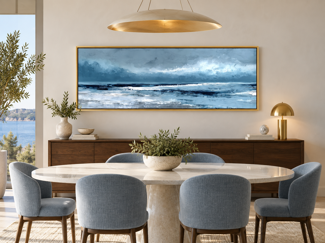 Long horizontal abstract blue ocean canvas wall art in a gold frame above a dining room sideboard.