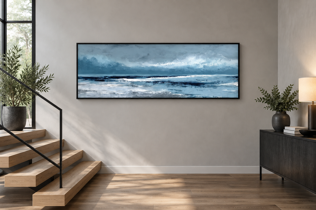 Long horizontal abstract blue ocean canvas wall art in a black frame above a wooden staircase.