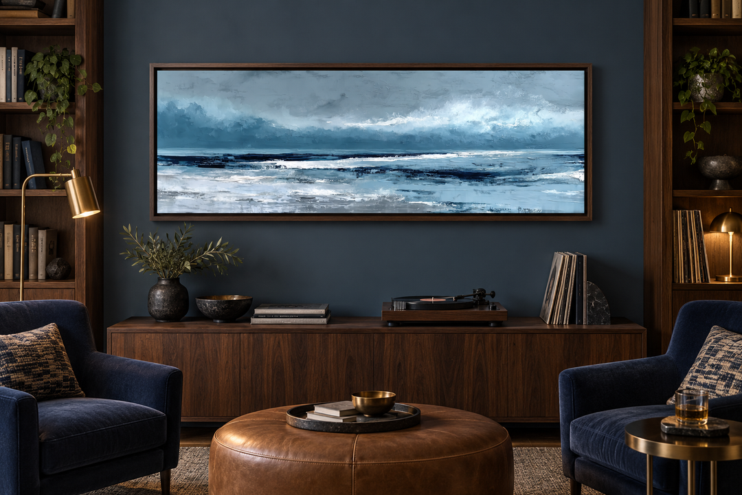 Long horizontal abstract blue ocean canvas wall art in a dark wood frame above a wooden sideboard.
