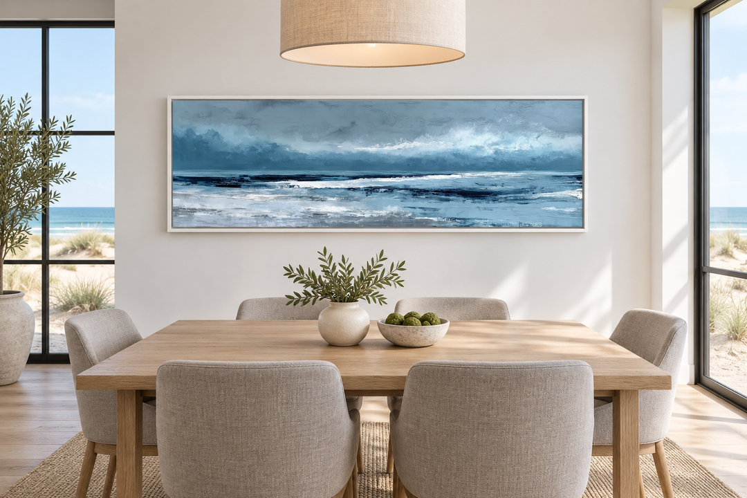 Long horizontal light blue abstract ocean canvas wall art above a dining table in a coastal room.