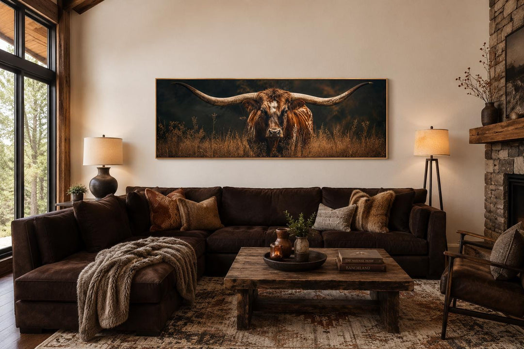 Longhorn Bull wall art with sweeping horns in golden grass above a brown sofa in a rustic room.