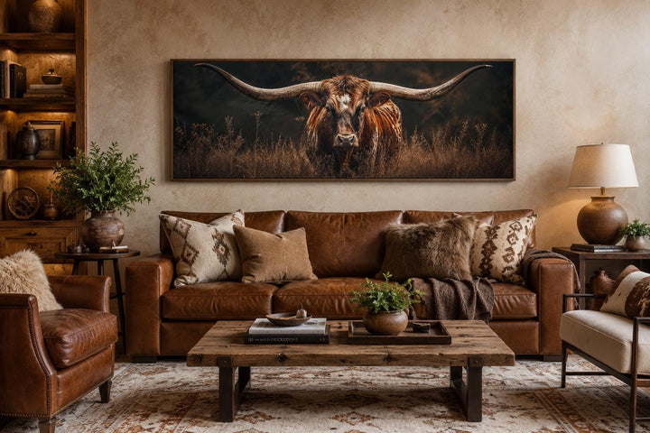 Longhorn Bull wall art with sweeping horns in golden grass above a brown leather sofa.
