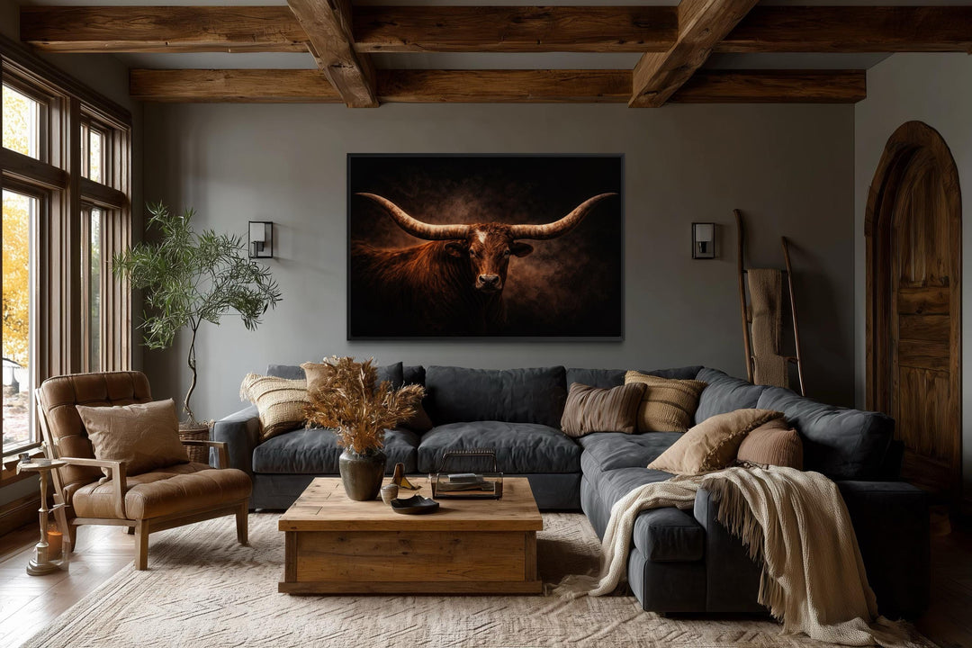 A large canvas print of a longhorn bull with wide horns hangs above a sofa in a rustic living room.