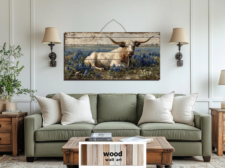Longhorn in bluebonnet field distressed wood wall art hanging above a green sofa in a farmhouse room.