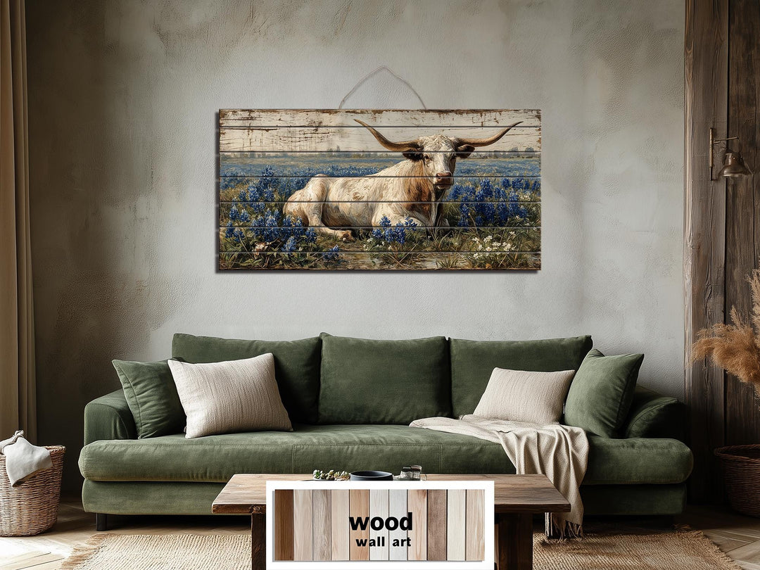 Longhorn in bluebonnet field distressed wood wall art hanging above a green sofa in a rustic room.