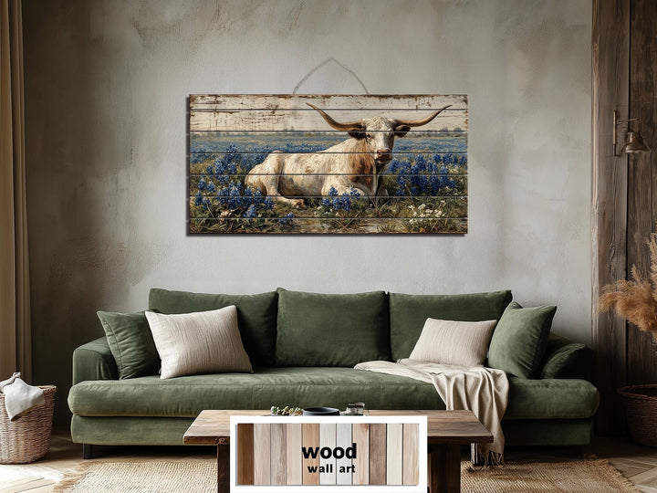 Longhorn in bluebonnet field distressed wood wall art hanging above a green sofa in a rustic room.