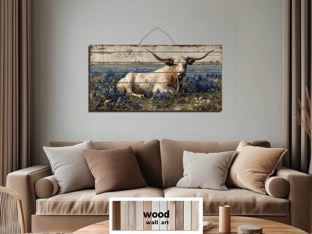 Longhorn in bluebonnet field distressed wood wall art hanging above a neutral sofa.