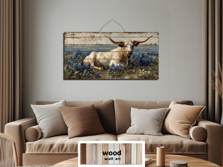 Longhorn in bluebonnet field distressed wood wall art hanging above a neutral sofa.