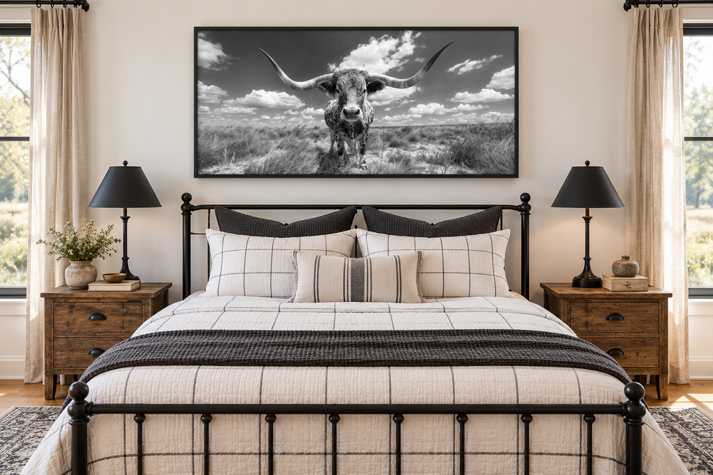 Black and white longhorn photography style framed canvas wall art hanging above a bed.