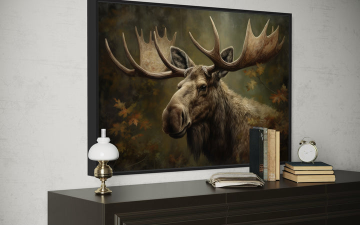 Framed canvas wall art of a majestic bull moose in an autumn forest displayed on a dark dresser.