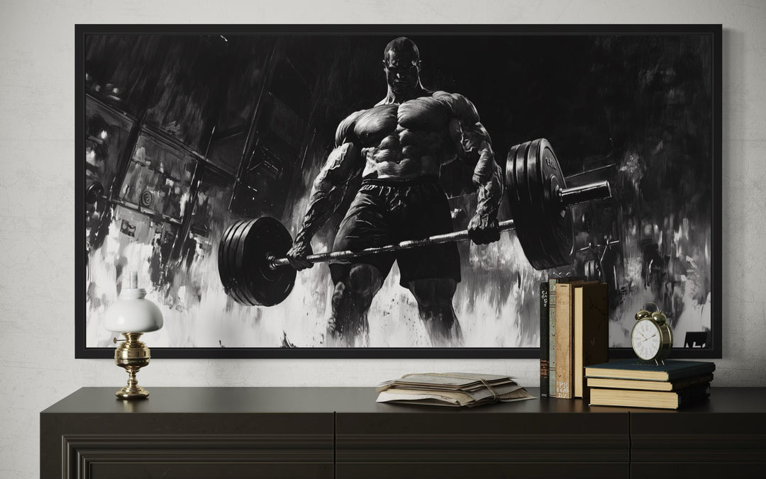 Black and white framed canvas art of a muscular man doing a deadlift, displayed above a dark dresser.