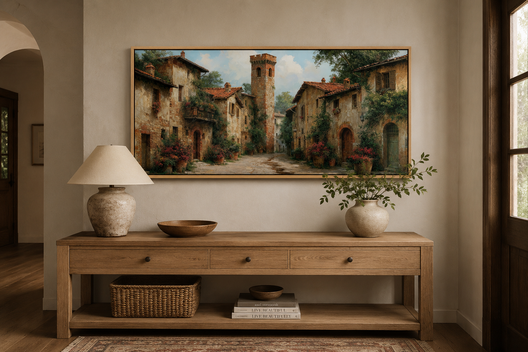 Framed wall art of a medieval village with stone cottages above a wooden console table.