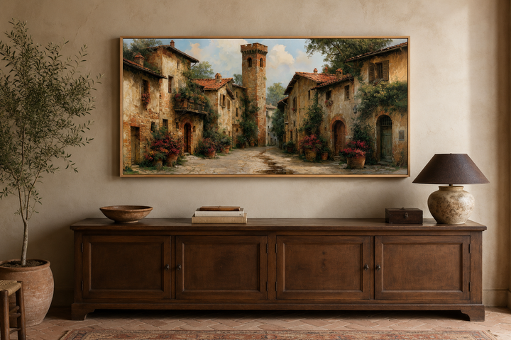 Framed wall art of a medieval village with stone cottages and a cobblestone path above a sideboard.