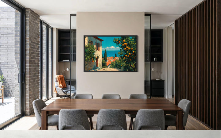 A framed canvas print of a Mediterranean village with orange trees hangs in a modern dining room.