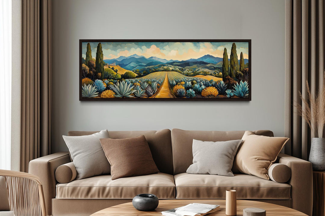 Panoramic canvas art of a Mexican agave field with golden paths and blue mountains over a sofa.
