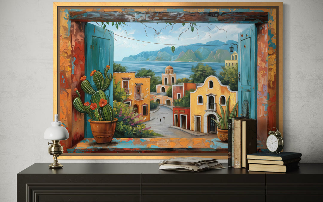 Framed canvas wall art of a Mexican village view through an open window with a cactus and sea.