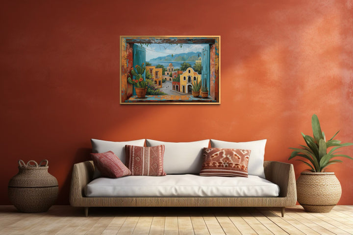 Mexican Village Window View Framed Canvas Wall Art hanging on a terracotta wall above a sofa.