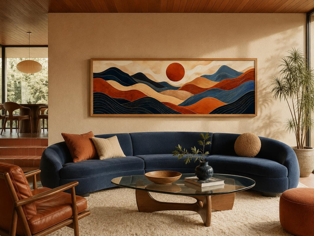 Long horizontal abstract mountain wall art in burnt orange and navy blue above a navy curved sofa.