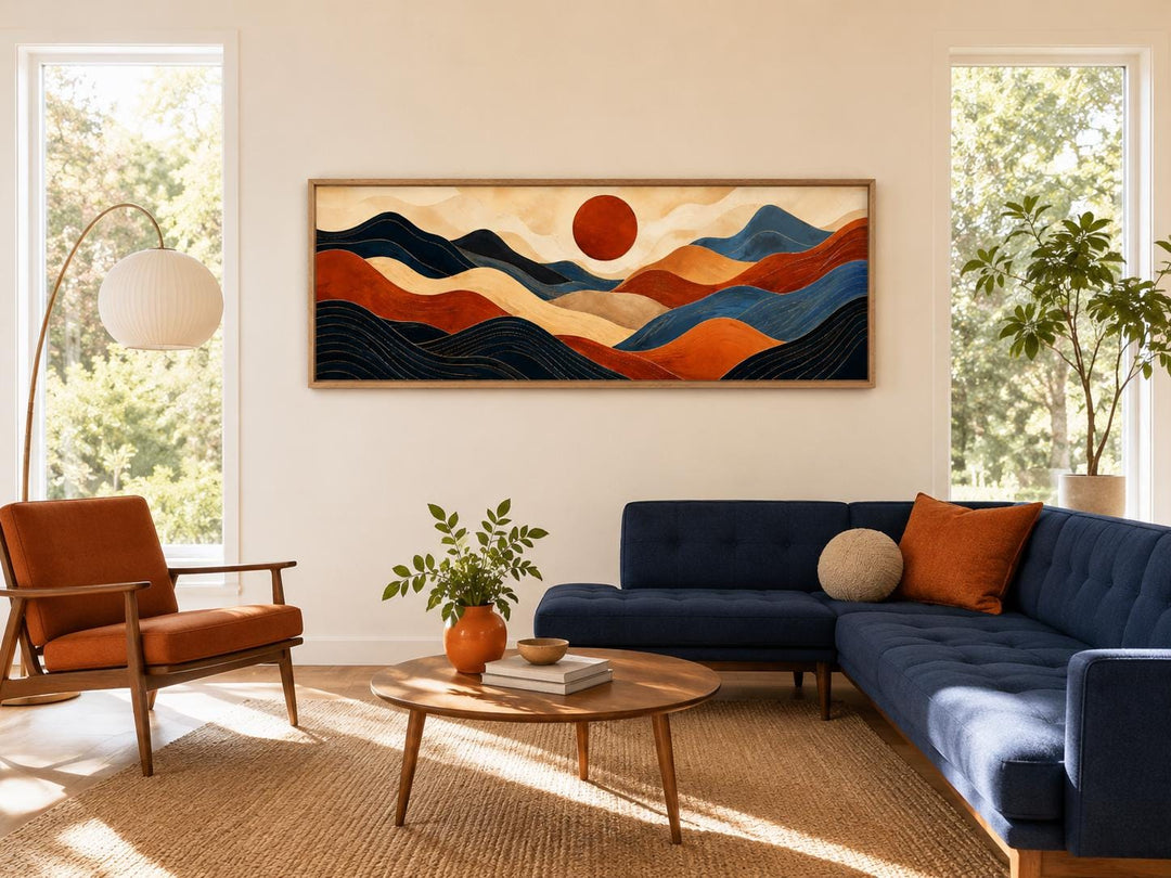Long horizontal abstract mountain wall art in burnt orange and navy blue above a navy sofa.