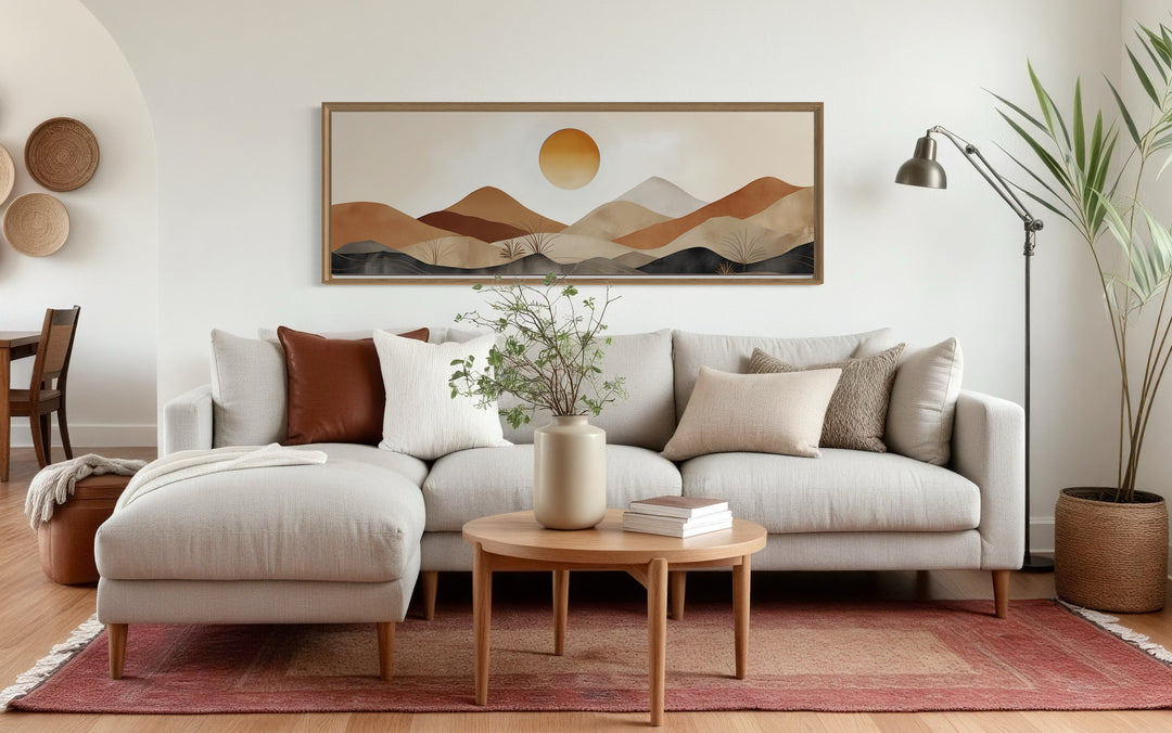 Long narrow canvas wall art of a neutral brown and beige mountain sunset landscape above a sofa.