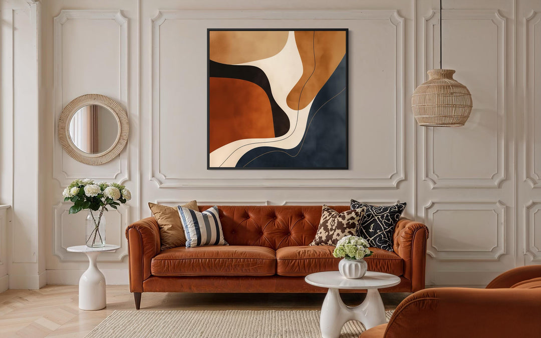 Square abstract canvas art with navy, rust, and beige organic shapes above a brown leather sofa.