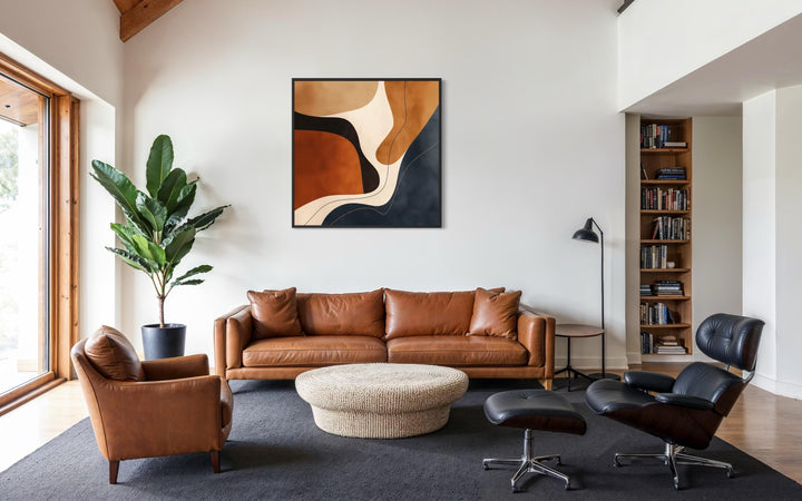 Square abstract canvas wall art with organic shapes in navy and earth tones above a leather sofa.