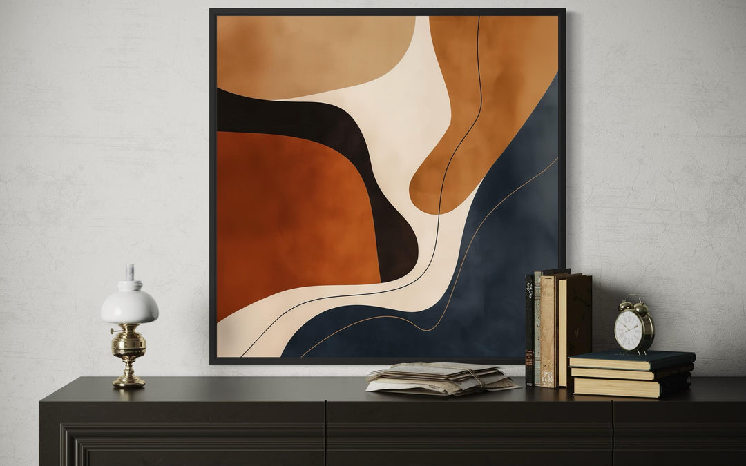 Square abstract canvas art with organic shapes in navy, rust, and beige on a dark wood console.