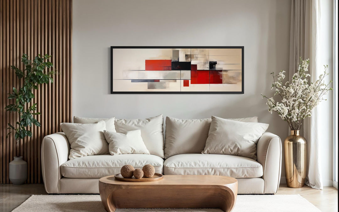 Large abstract geometric canvas print in red, beige, and black hanging above a modern sofa.