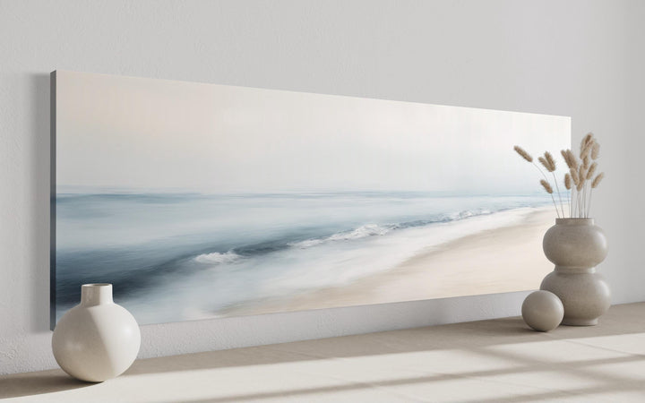 Panoramic minimalist watercolor ocean beach wall art in soft blue and gray tones on a white wall.