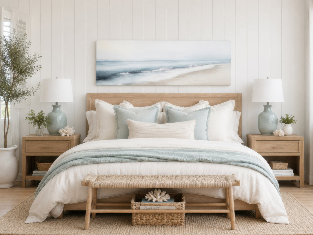 Panoramic watercolor ocean beach painting in gray and blue tones above a bed in a coastal bedroom.