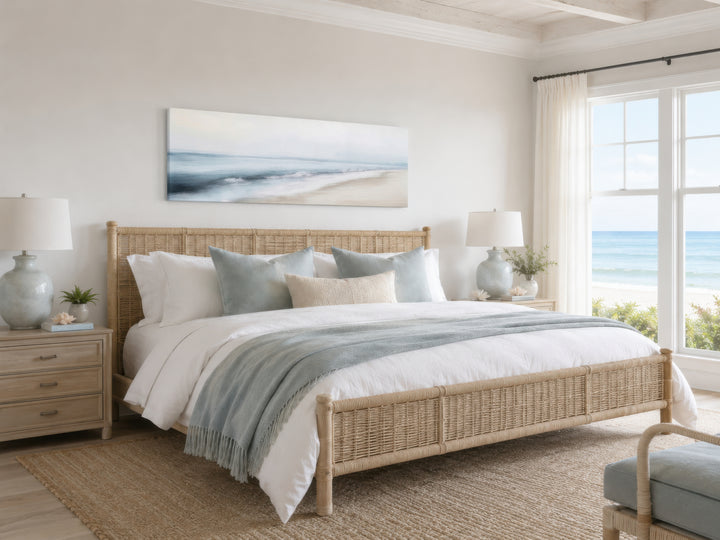 Minimalist coastal gray blue watercolor panoramic ocean beach painting above a woven bed frame.
