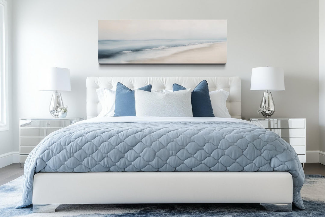 Minimalist panoramic coastal wall art of a gray and blue watercolor ocean beach above a bed.