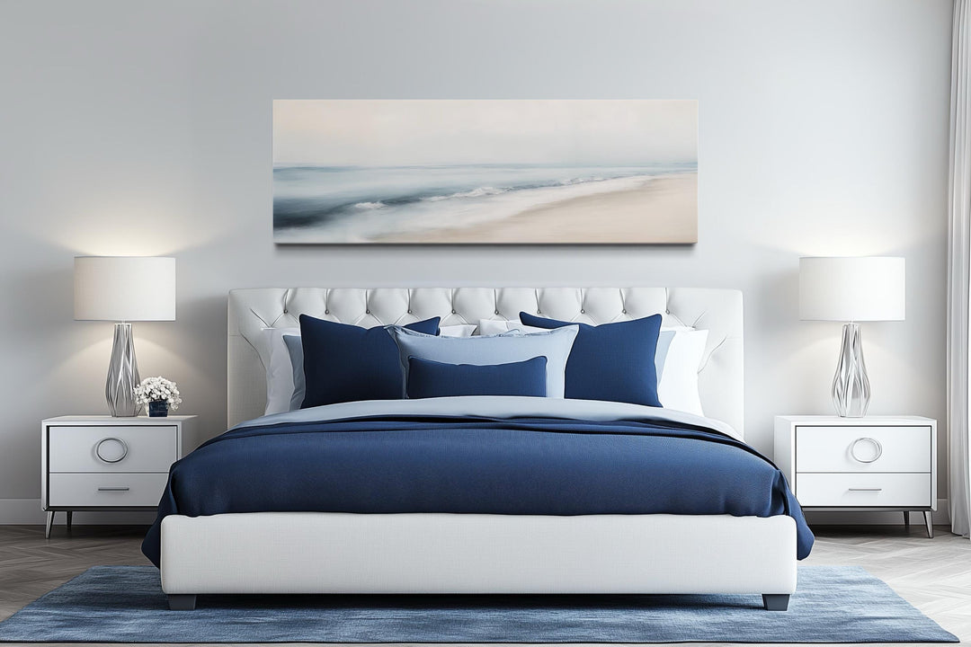 Minimalist panoramic watercolor ocean beach canvas art hanging above a white tufted bed.