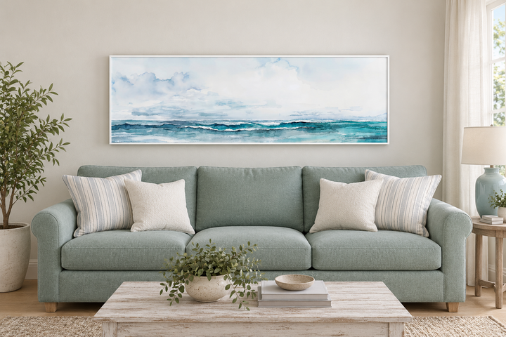 Minimalist horizontal framed canvas wall art of a blue and gray ocean scene over a seafoam sofa.